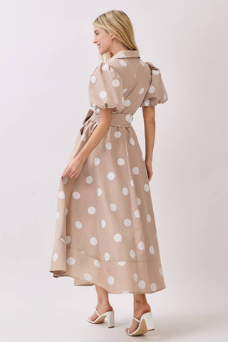 Woman wearing a beige dress with white polka dots on a plain background