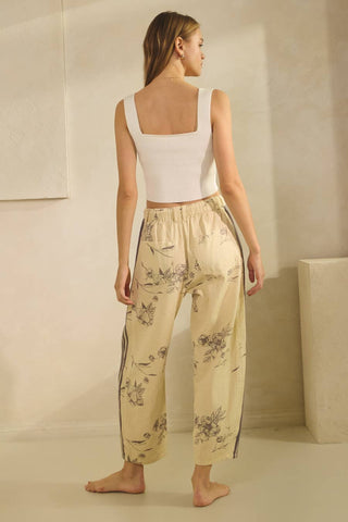 Woman wearing a white top and beige floral pants in a minimalistic setting