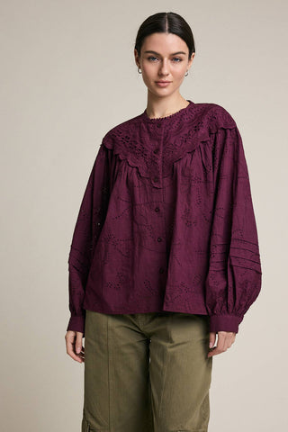 Woman wearing a burgundy blouse with lace details on a beige background