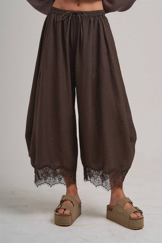 Brown wide-leg pants with lace trim worn by a person on a plain background