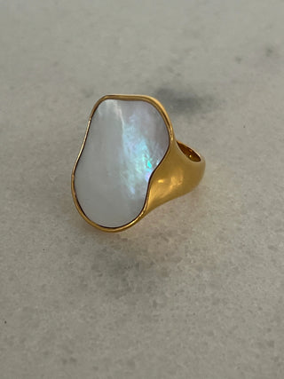 Gold ring with a white stone on a light gray background