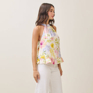 Woman wearing a floral halter top and white pants on a plain background