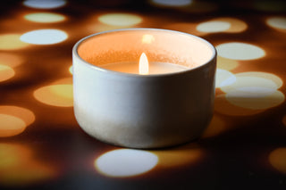 Candle in a white ceramic holder with a blurred bokeh background