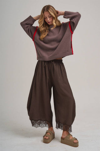 Woman wearing a brown sweater and wide-leg pants with lace trim on a white background