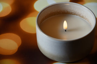 Candle in a white ceramic holder with a blurred warm-toned background