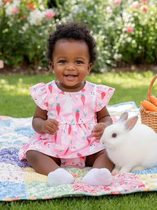 Child in a pink dress with a rabbit on a colorful blanket outdoors