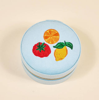 Round light blue jewelry box with embroidered fruits on a beige background