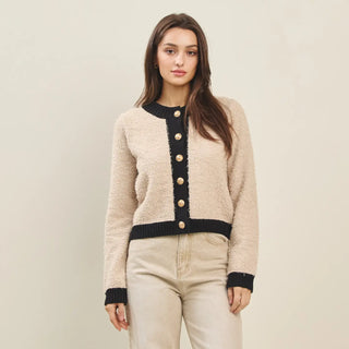 Woman wearing a beige cardigan with black trim against a plain background