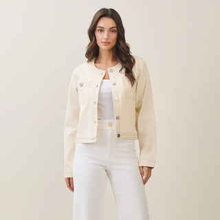 Woman wearing a beige denim jacket and white pants against a plain background