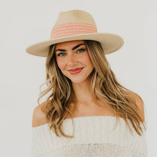 Woman wearing a straw hat with a pink band against a plain background