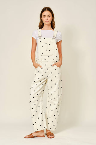 Woman wearing white polka dot overalls on a plain background
