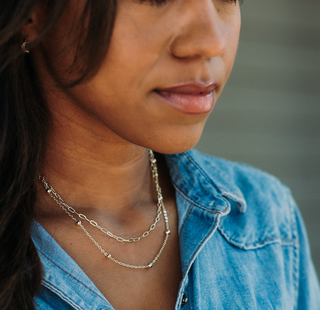 Woman wearing a blue denim shirt and layered necklaces with a blurred background