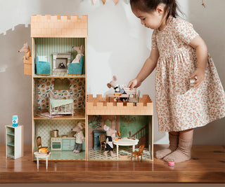 Child playing with a wooden dollhouse in a room.