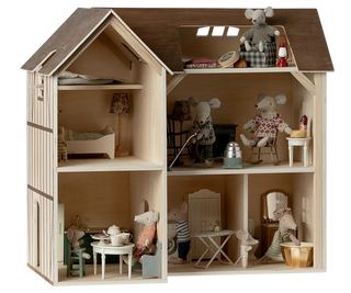 A wooden dollhouse with an open front and side, showcasing multiple miniature rooms furnished with tiny tables, chairs, lamps, and clothing. Several small plush mouse figures are arranged throughout the interior and on the roof, all photographed against a clean white background.