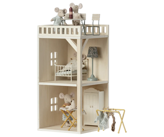 A light natural wood dollhouse with two floors and a balcony, furnished with small toy furniture, a lamp, and plush mouse figures, shown on a plain white background.