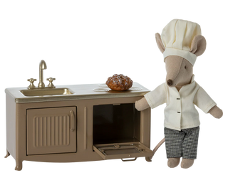 Stuffed animal chef character next to a toy kitchen set on a white background
