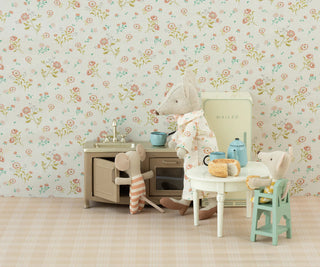 Children's play kitchen set with toys against a floral wallpapered wall.