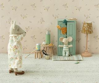 Two toy mice in a room with floral wallpaper, a lamp, and small furniture.
