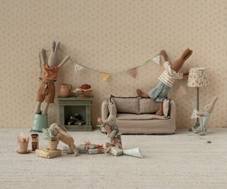Miniature room setup with toy figures and furniture against a beige wall.
