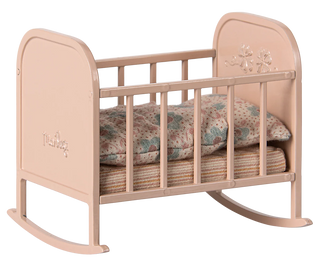 Pink baby crib with floral bedding on a white background