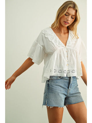 Woman wearing a white blouse with lace details and denim shorts on a light background
