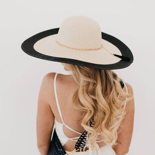 Woman wearing a wide-brimmed hat with a black band on a plain background