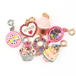 A set of six colorful birthday-themed charms and keychains arranged on a plain white background. The charms include a pink 'HAPPY BIRTHDAY' round charm, a red rhinestone heart charm reading 'OCTOBER', a pink cupcake charm, a silver glitter cupcake charm, a gold '9' charm, and a tiered birthday cake charm.