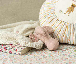 Pink plush toy and striped pillow on a floral blanket with a neutral background