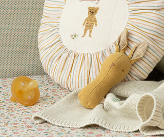 Baby items including a pacifier, plush toy, and blanket on a patterned surface.