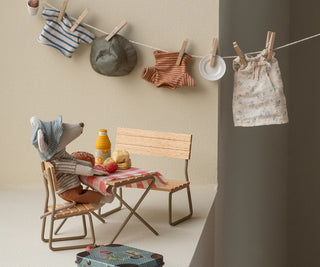 Miniature setup with a chair, table, and clothes hanging on a line against a neutral wall.