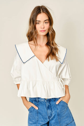 Woman wearing a white blouse with blue trim and blue jeans on a beige background