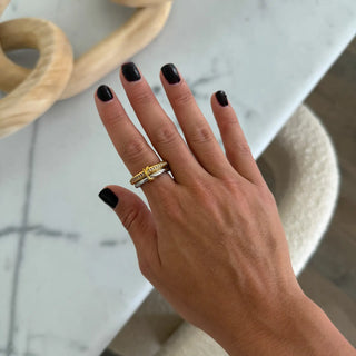 Hand with black nail polish wearing two gold rings on a marble surface