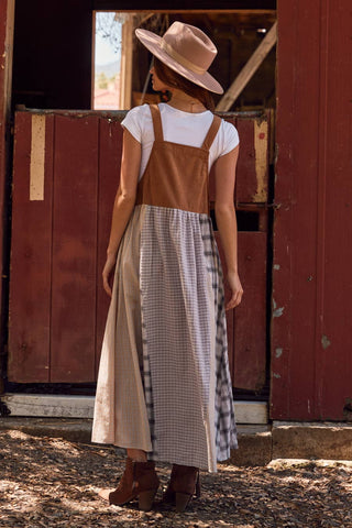 Woman wearing a white shirt, brown overalls, and a beige hat standing in front of a red barn.