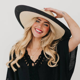 Woman wearing a large black and beige hat against a plain background