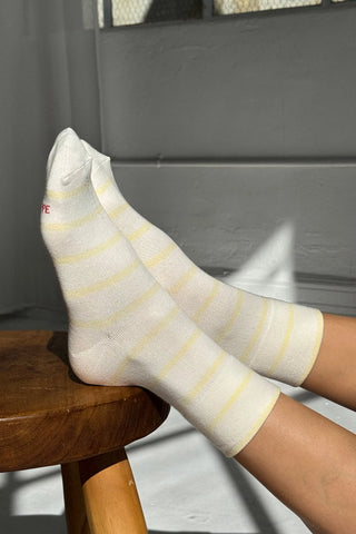 White socks with yellow stripes on a wooden stool against a gray wall.