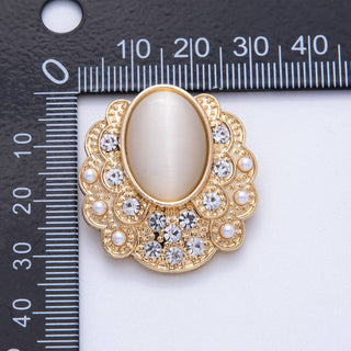 Decorative brooch with gold frame and central stone on a white background with ruler for scale.