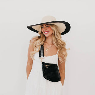 Woman wearing a wide-brimmed hat and white dress with a black bag on a plain background
