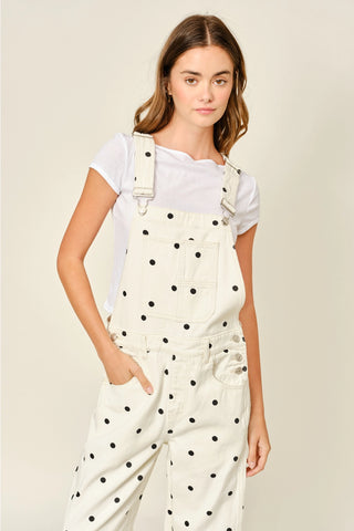 Woman wearing a white polka dot jumpsuit with a plain background