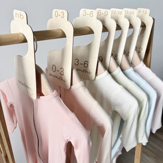Baby clothes on hangers with size labels on a wooden rack.