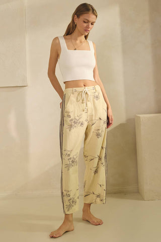 Woman wearing a white top and beige floral pants against a neutral background