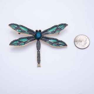 Dragonfly-shaped brooch with teal and gold details next to a quarter for scale on a white background