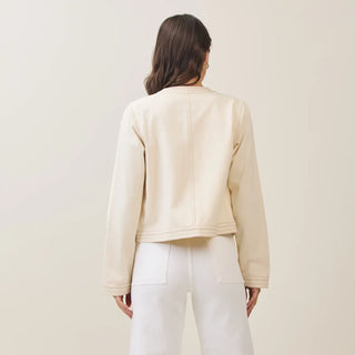 Person wearing a beige jacket and white pants against a plain background