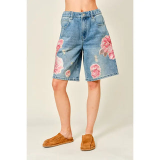 Denim shorts with floral patterns worn by a person on a plain background