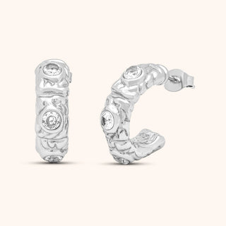 Silver hoop earrings with intricate designs and clear gemstones on a white background