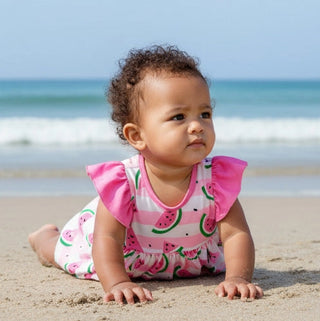 Baby in a pink and white swimsuit with watermelon pattern on a beach
