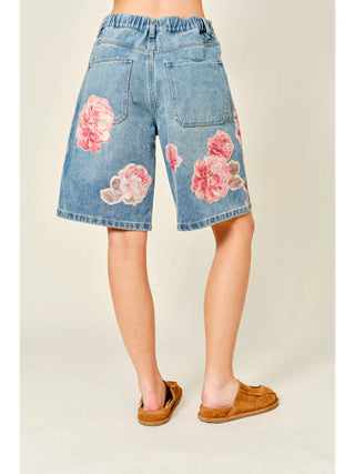 Denim shorts with floral patterns worn by a person on a plain background