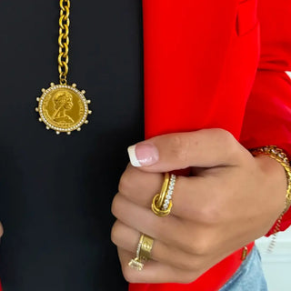 Hand wearing gold rings with a gold pendant against a red and black background