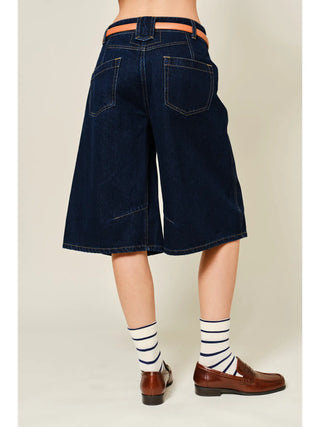 Person wearing dark blue denim shorts with a plain background