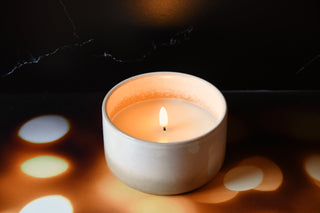 Candle in a white ceramic holder on a dark surface with light reflections
