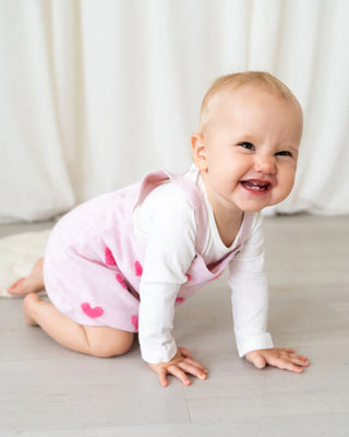 Baby in a pink onesie with heart patterns on a light background